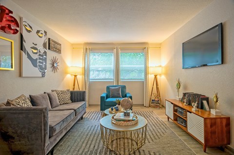 Living room in the Canvas East Nashville Apartments with midcentury modern decor, large couch, and double wide windows with blinds and curtains.